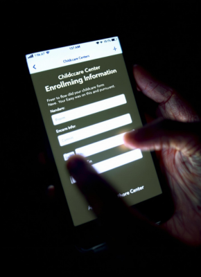 A person using a smartphone to fill out an online enrollment form for a childcare center in a dimly lit setting.